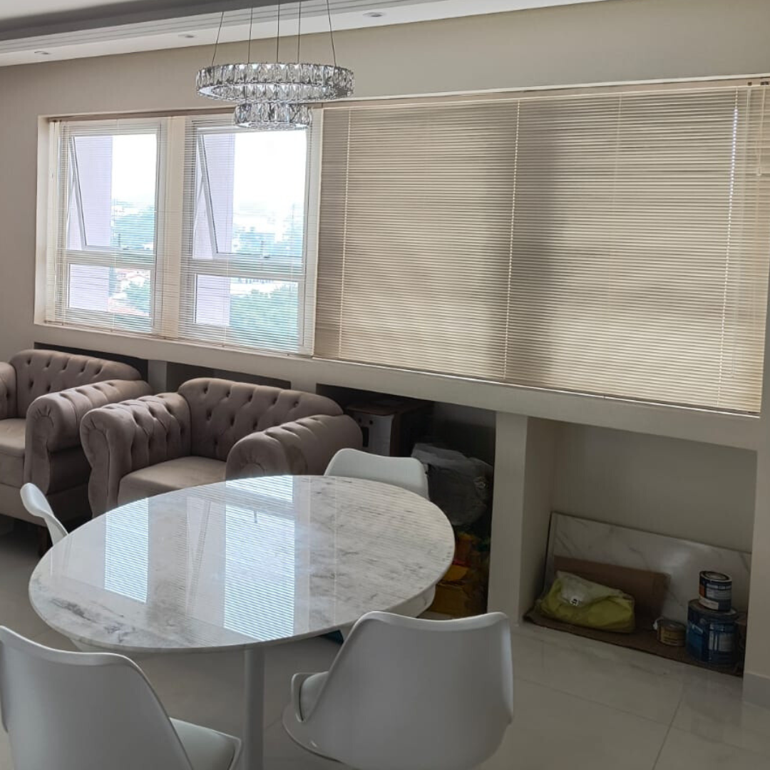 Uma sala de jantar com uma mesa redonda, persianas e cadeiras