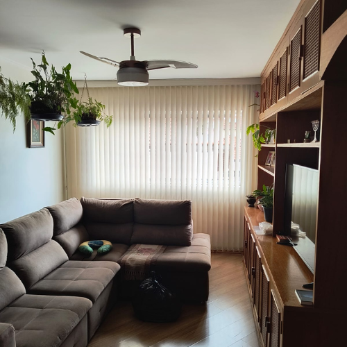 Uma sala de estar com um sofá secional, persianas e um ventilador de teto