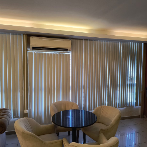 Uma sala de estar com uma mesa redonda, persianas e cadeiras