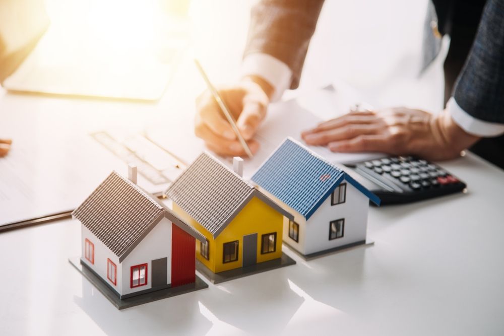 Miniature houses with a person signing documents near a calculator.