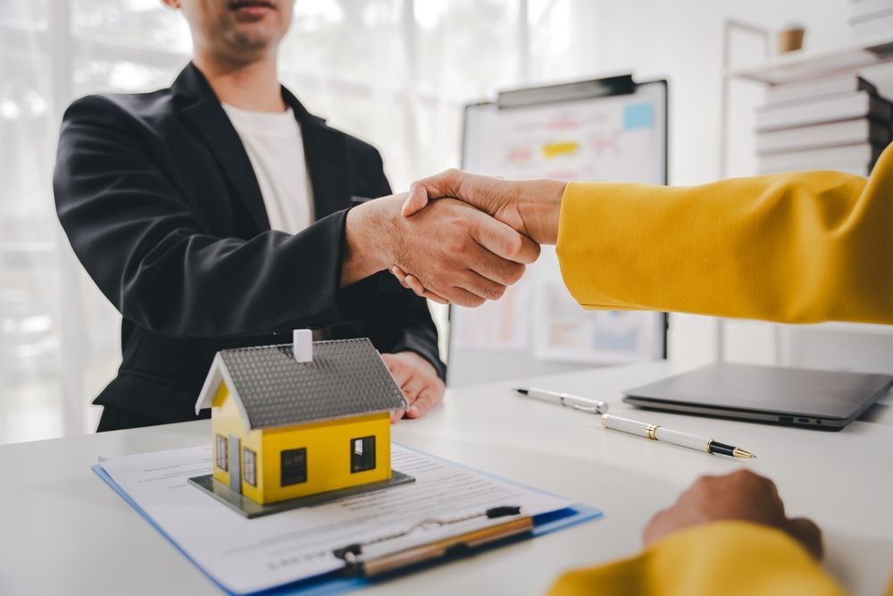 Man and person shaking hands over a contract and a model house on a desk.