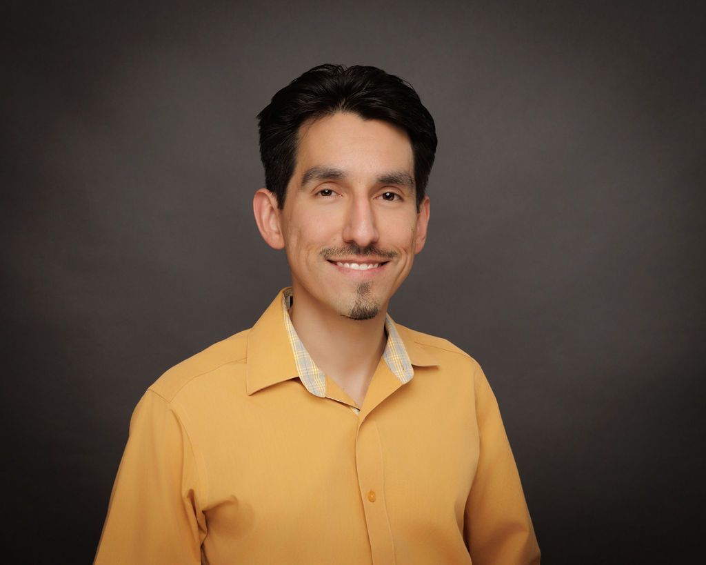 Richard-Michael Calzada, MS, LPC with dark hair and beard wearing a blue polo shirt smiling in a chair.