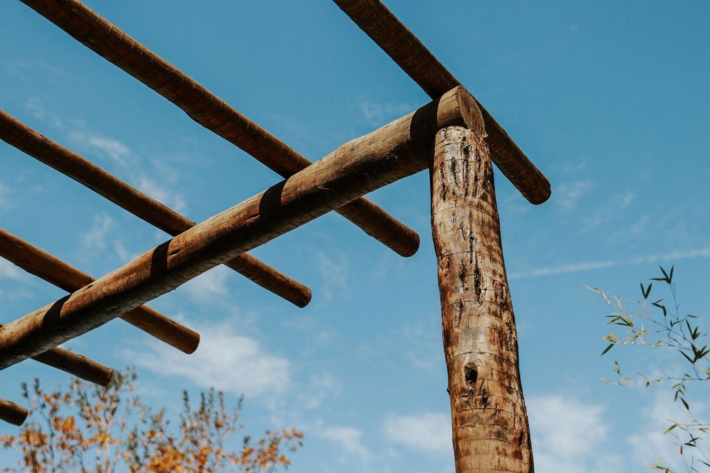 Uma pérgola de madeira com um céu azul ao fundo.