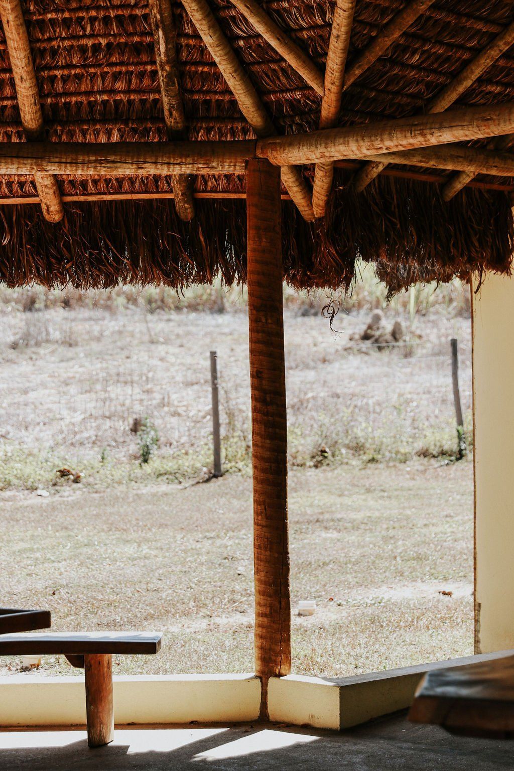 Uma varanda de madeira com telhado de palha e um banco.