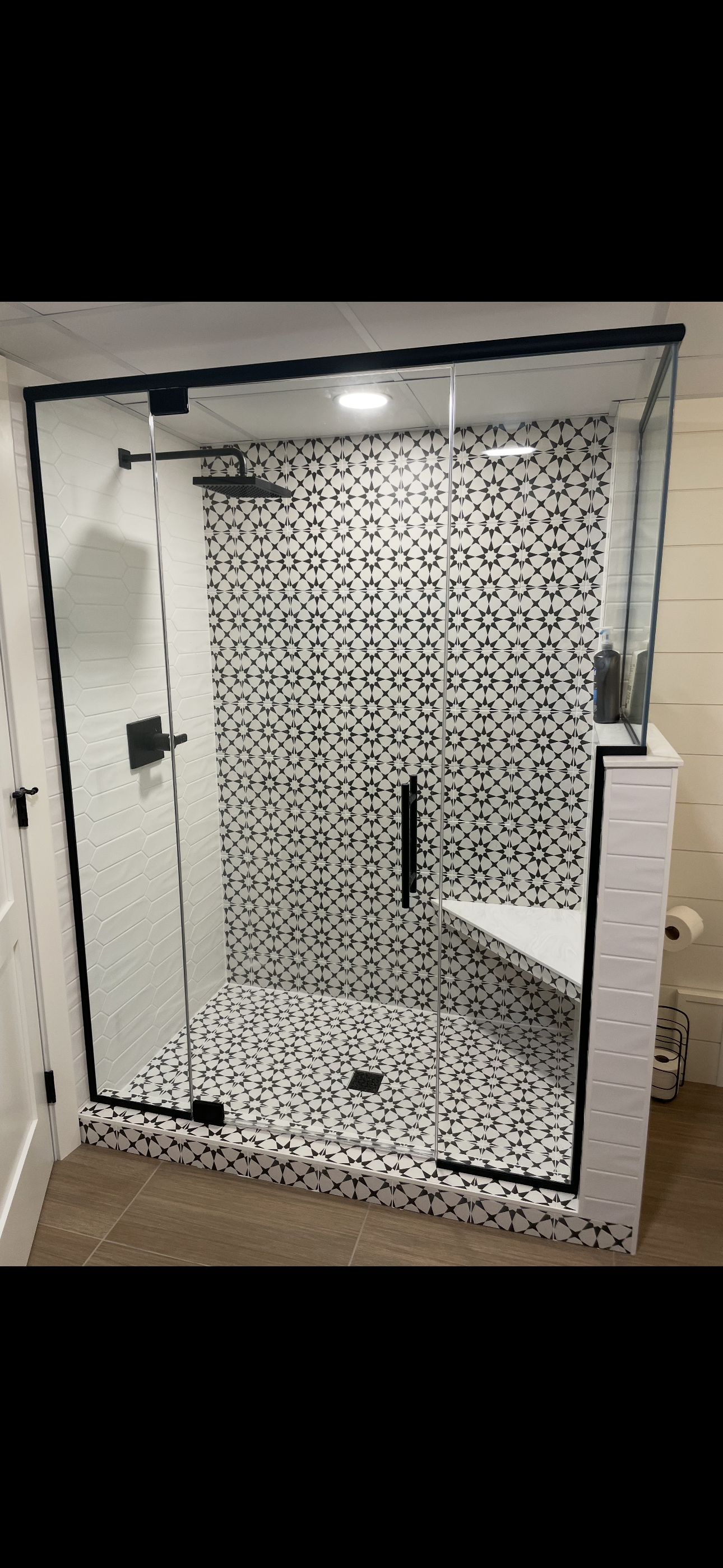 A bathroom with a walk in shower with a black and white tile wall.