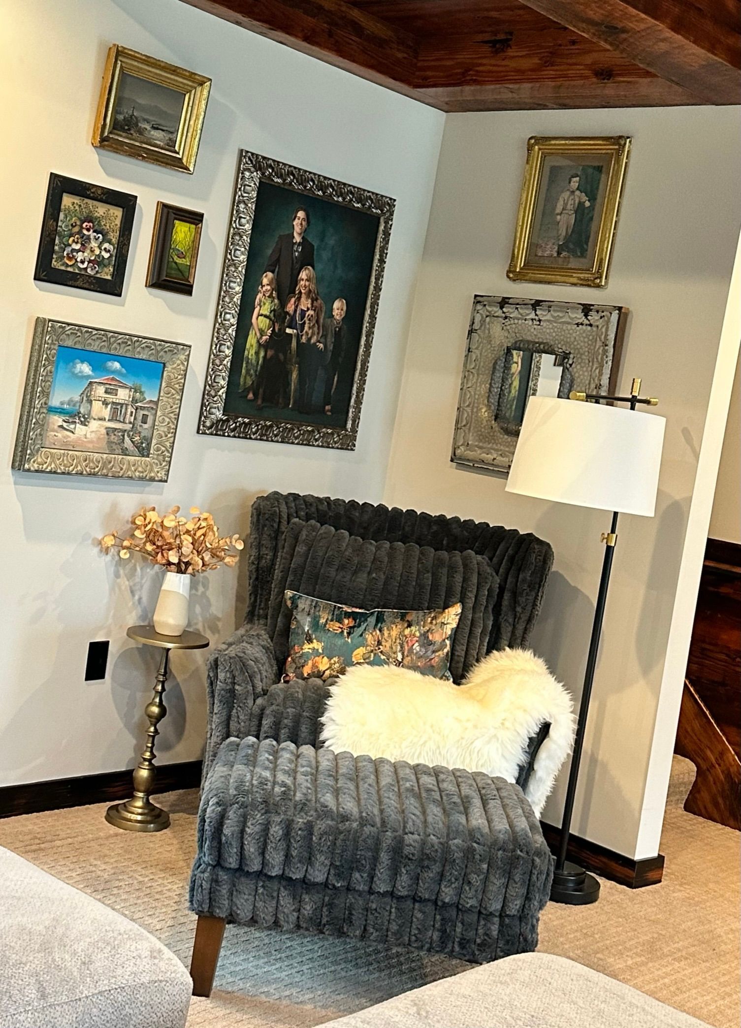 A living room with a chair , ottoman , lamp and paintings on the wall.