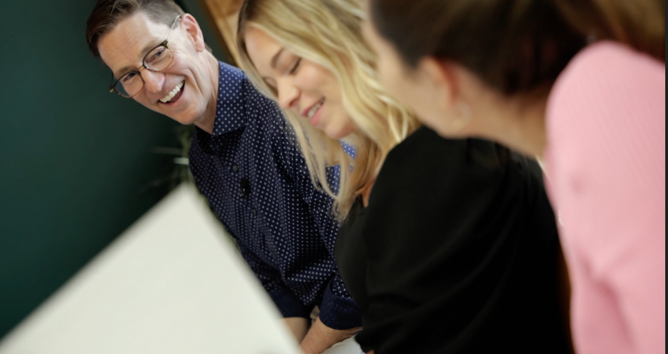 A group of people are sitting around a table and smiling.