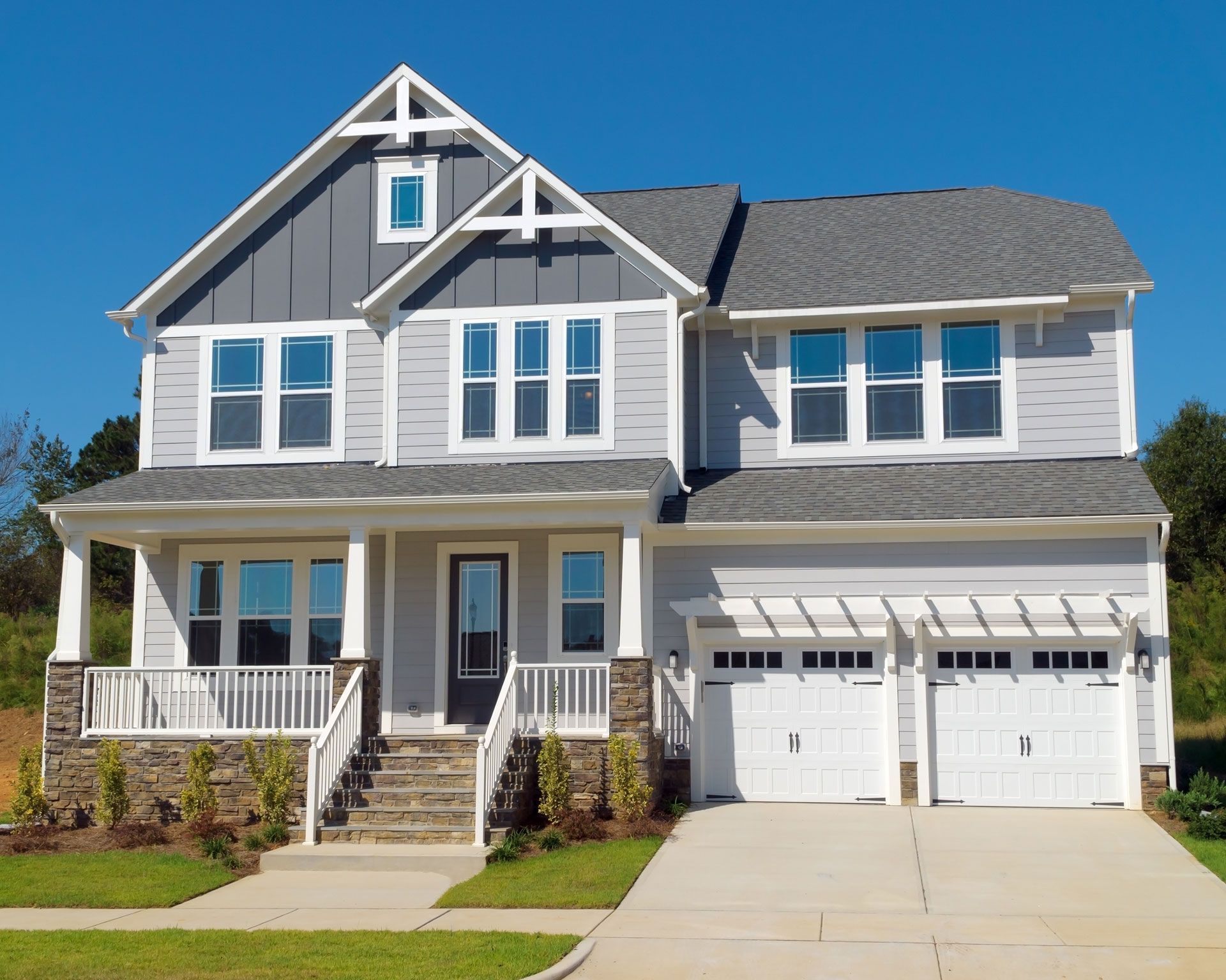 Two-story gray house with white trim and garage, blue sky in the background. Front porch with stairs and stone accents.