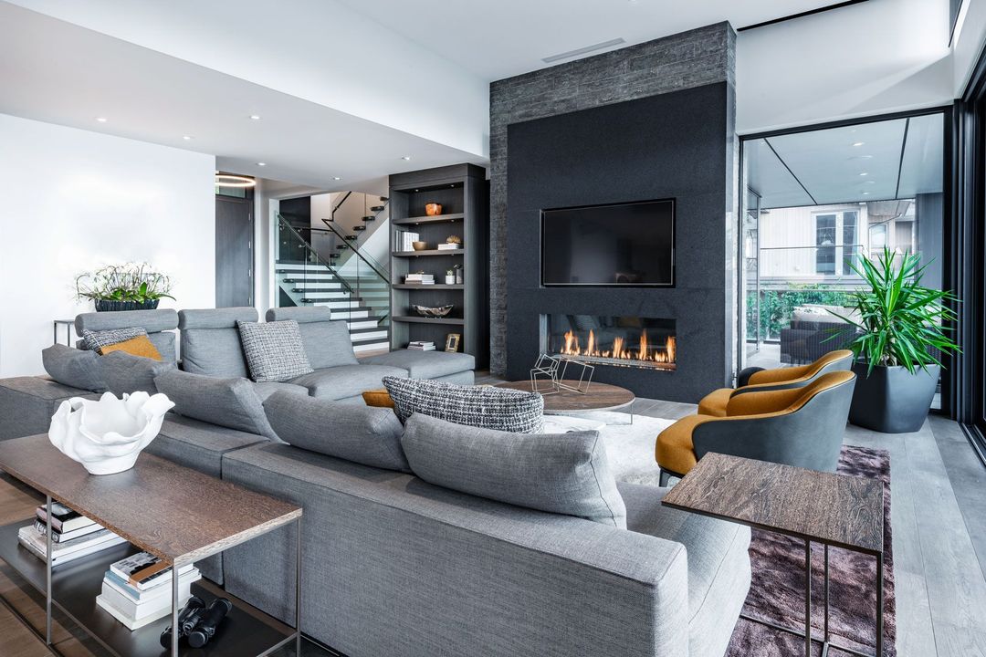 Modern living room with gray sectional sofa, fireplace, and glass doors leading to a balcony.