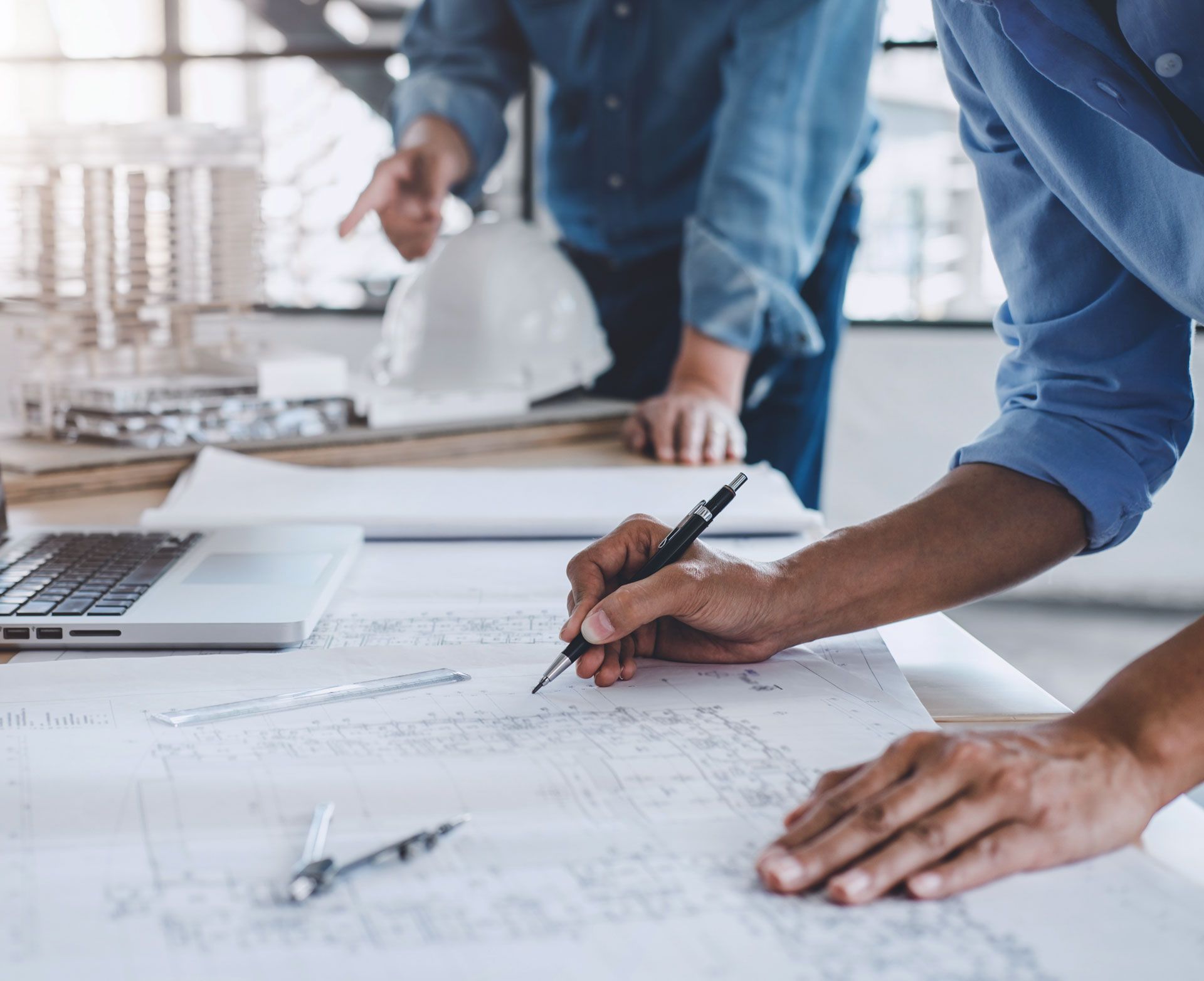 Two architects collaborating over blueprints, one pointing, the other writing.