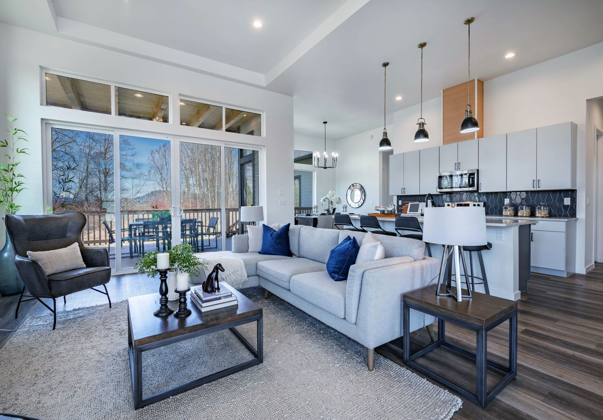Spacious, modern living room and kitchen with a large sectional, open to an outdoor deck. Neutral colors with blue accents.