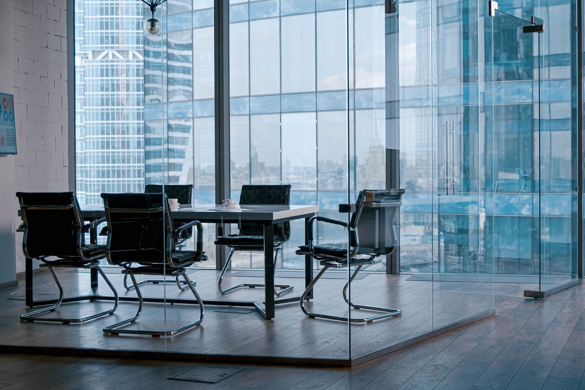 Conference room with a large window overlooking a city skyline; a table and chairs are set up for a meeting.