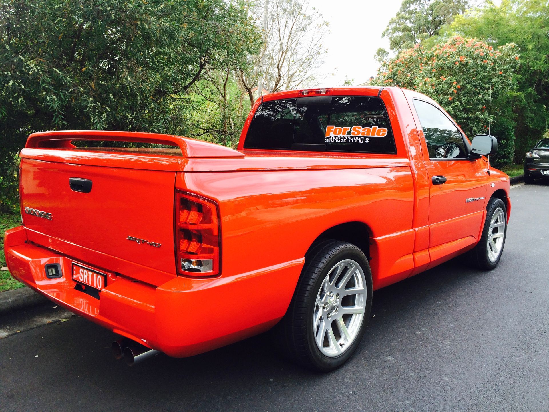Bright orange Dodge Ram pickup truck with chrome wheels parked on a street.