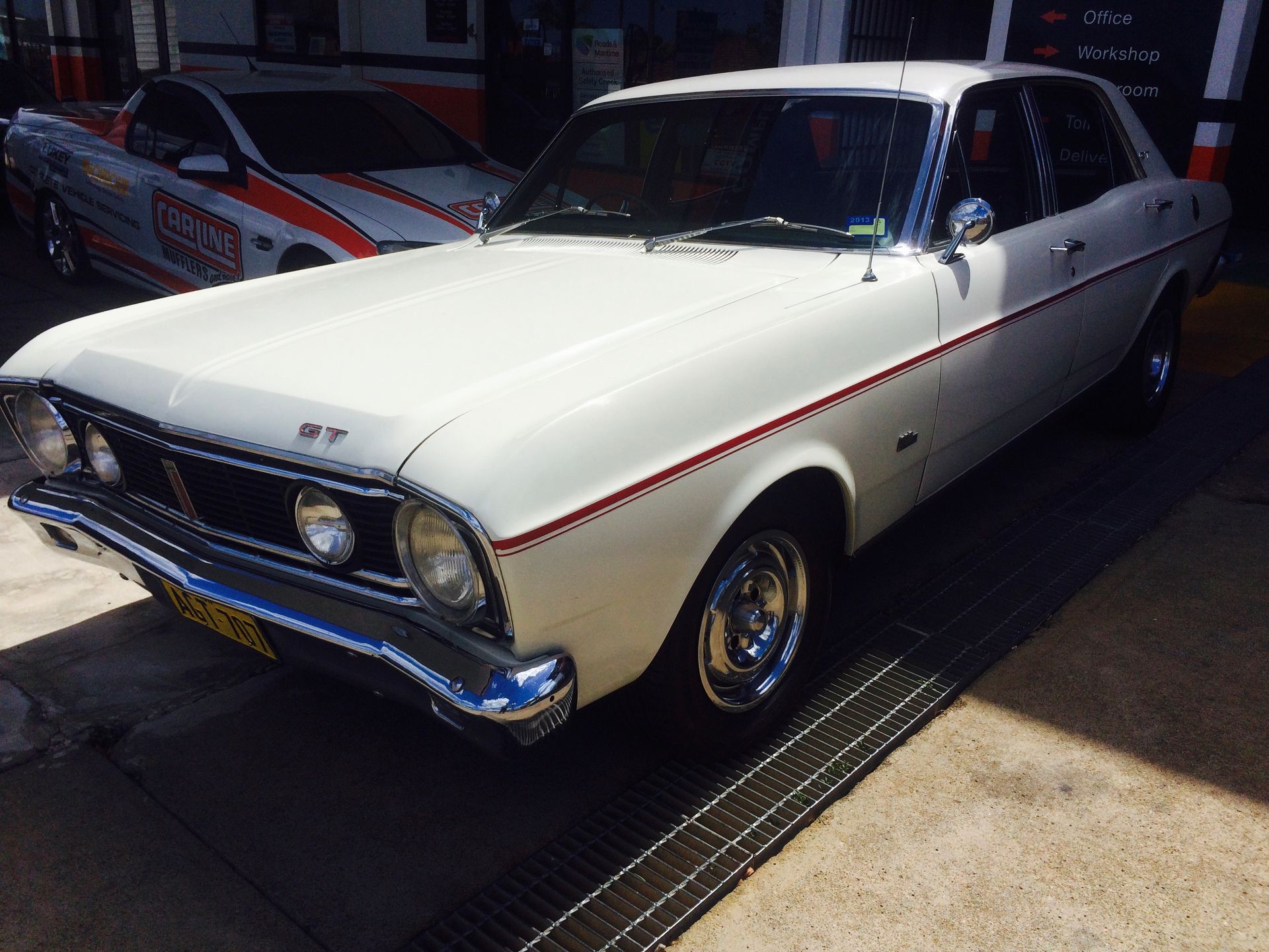 White vintage Ford Falcon GT parked outdoors with red trim.