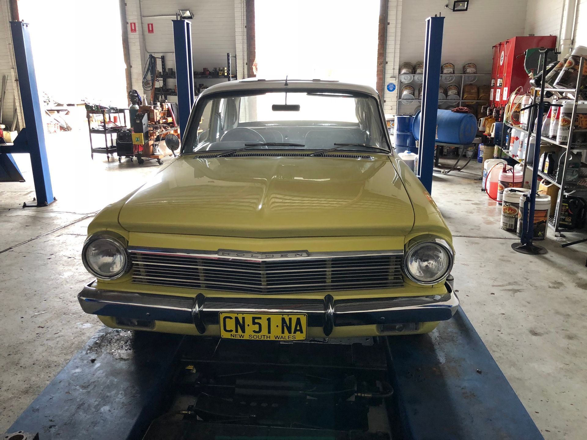 Yellow vintage car on a lift in a garage, CN 51 NA license plate.