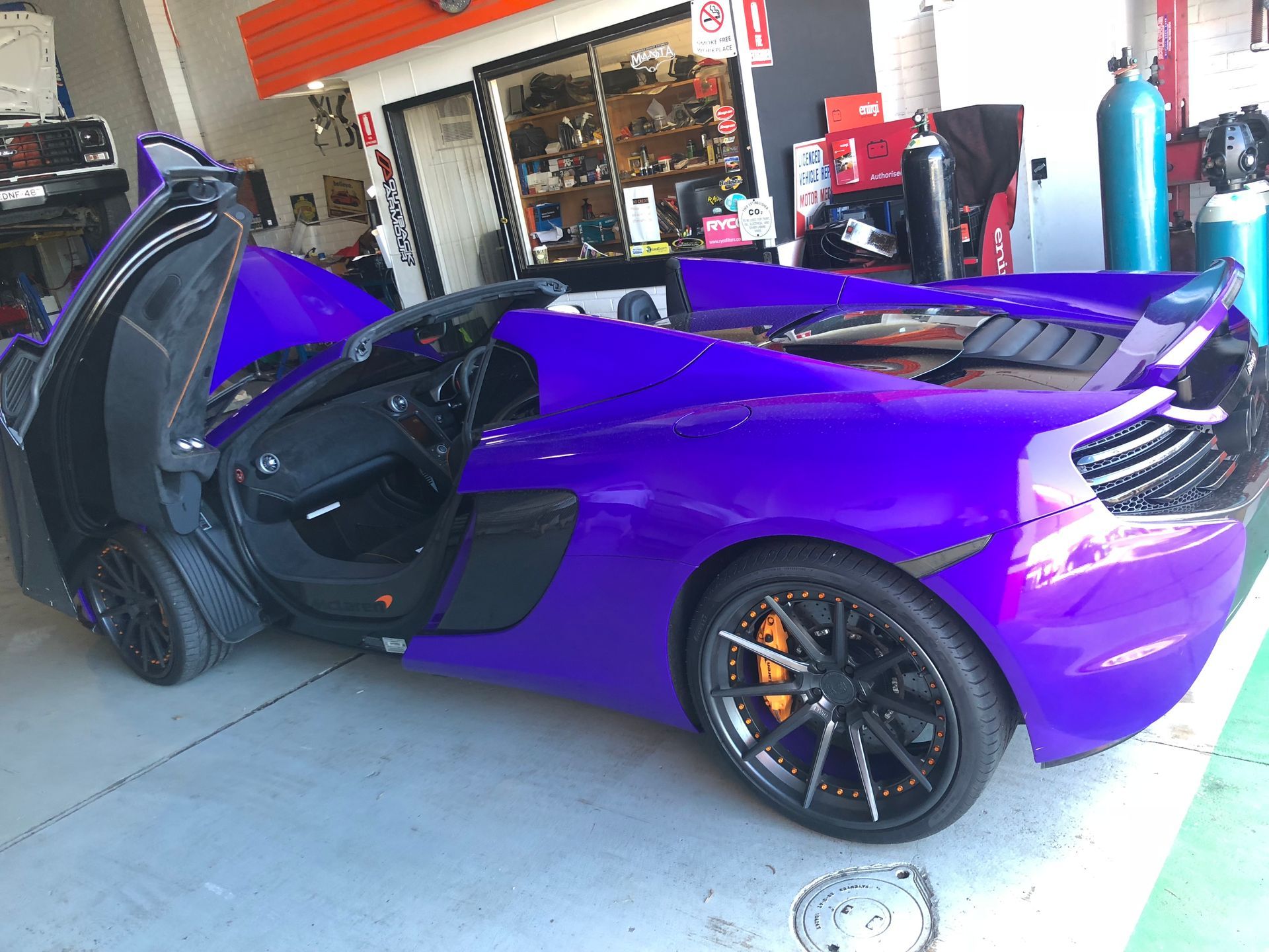 Purple sports car with doors open, in a garage.