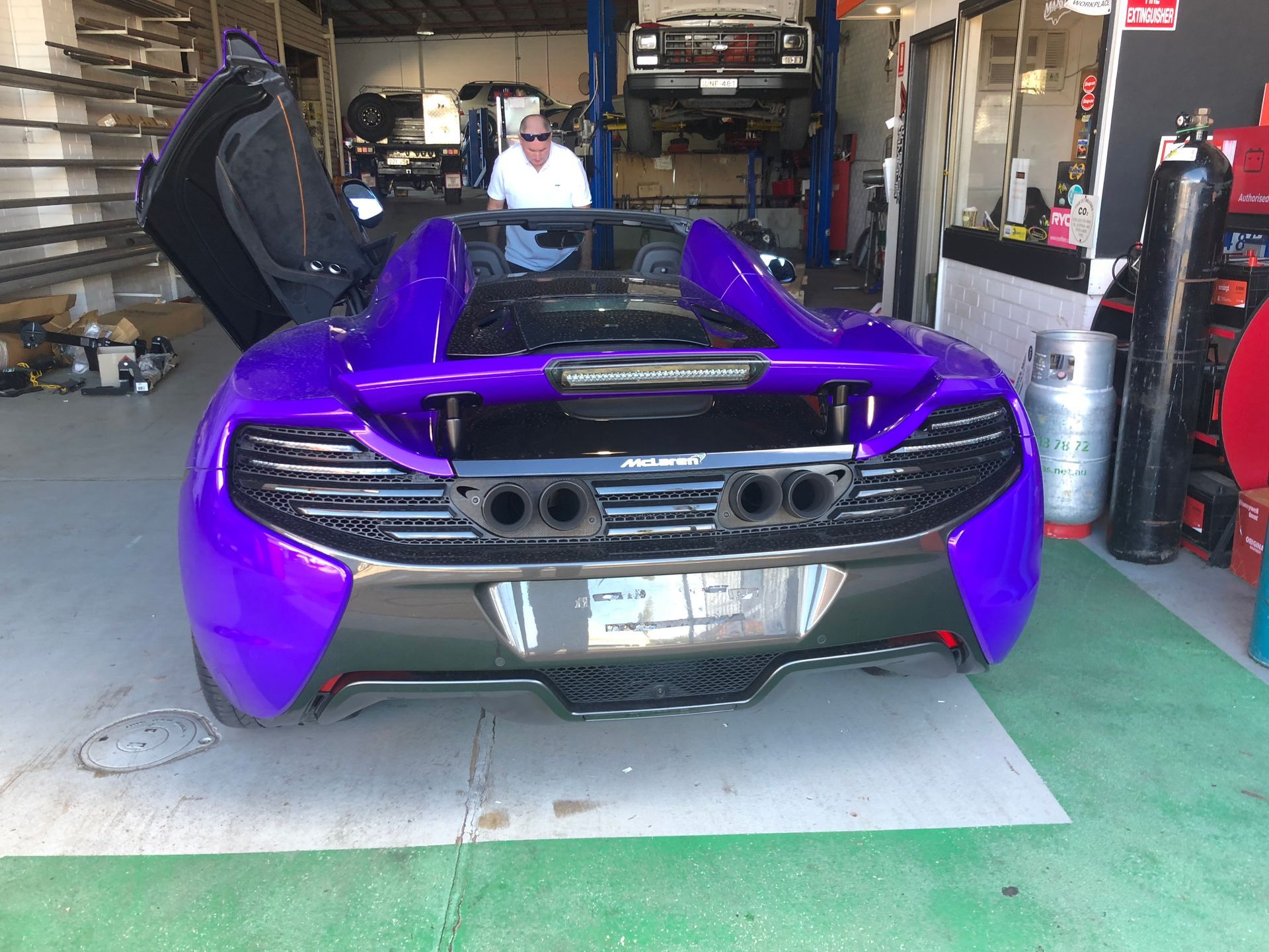 Purple McLaren sports car with open doors in a garage, man in background.