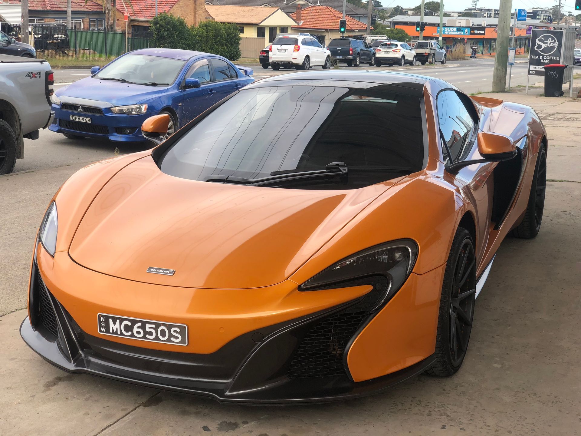 Orange McLaren 650S sports car parked on a street with other vehicles.