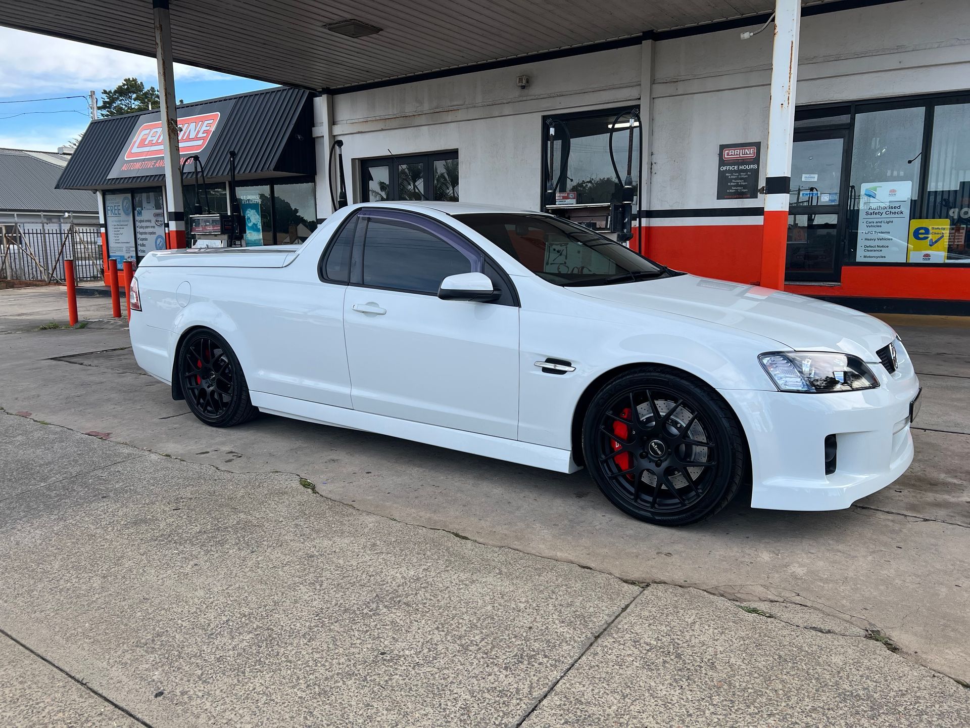 White ute with black rims parked at a gas station, red brake calipers visible.