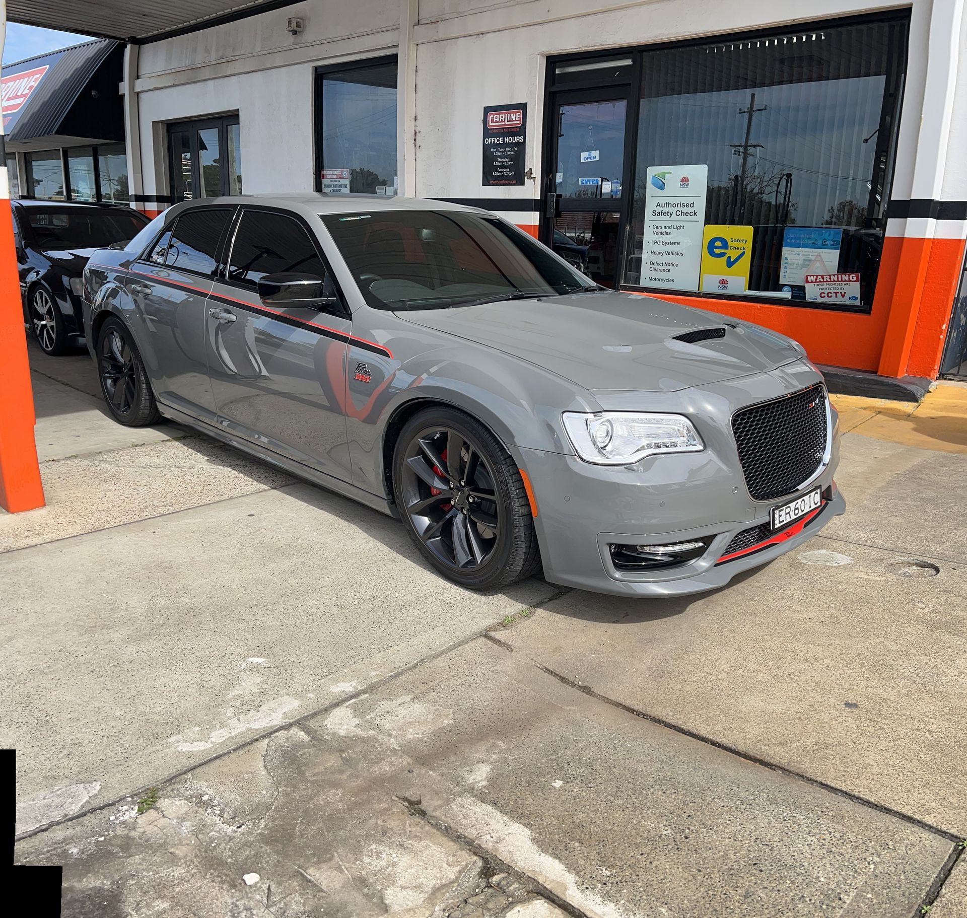 Gray Chrysler 300 sedan parked in front of a shop; red and black trim.