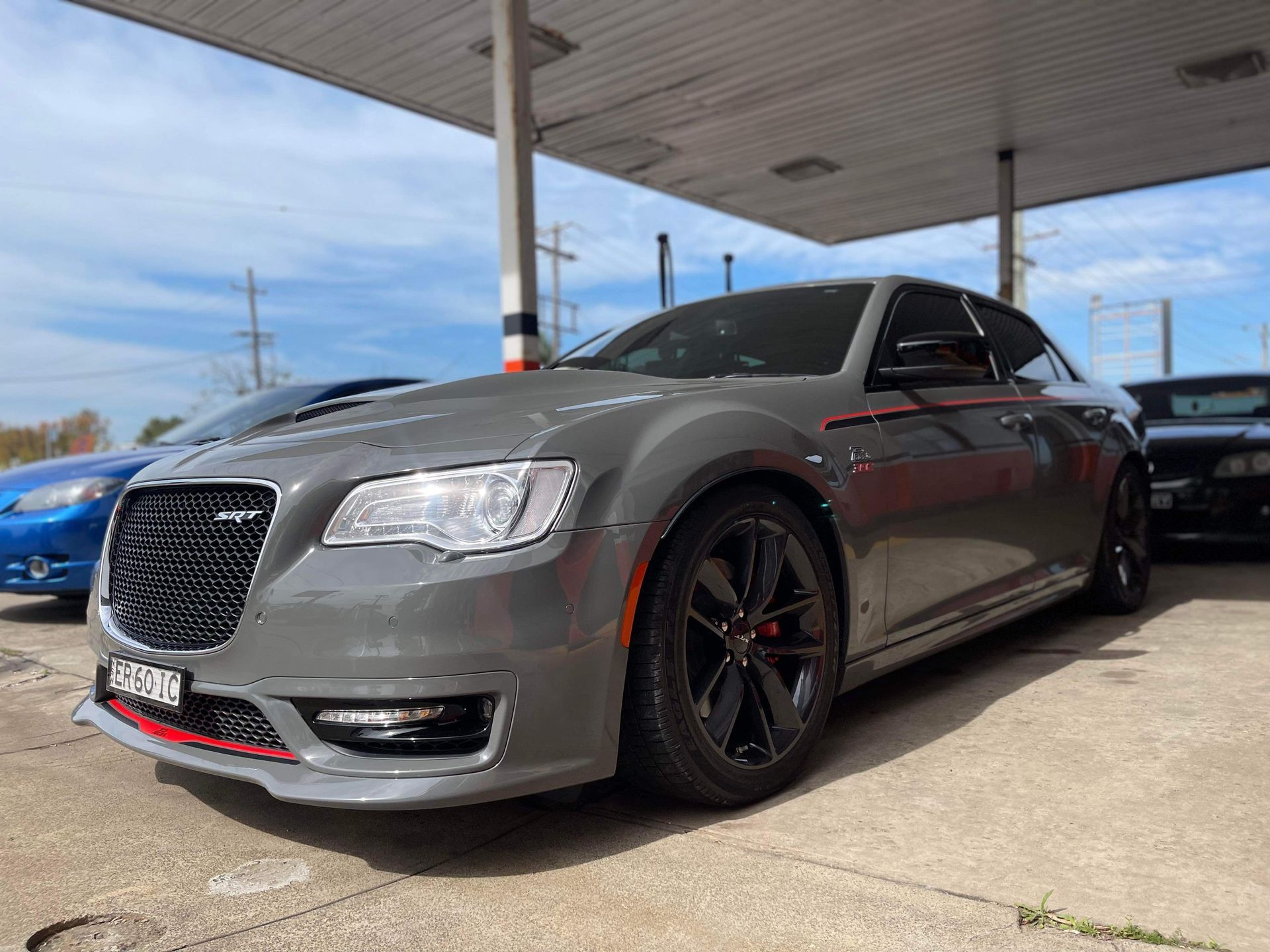 Gray Chrysler 300 with black rims at a gas station, under a white canopy on a sunny day.