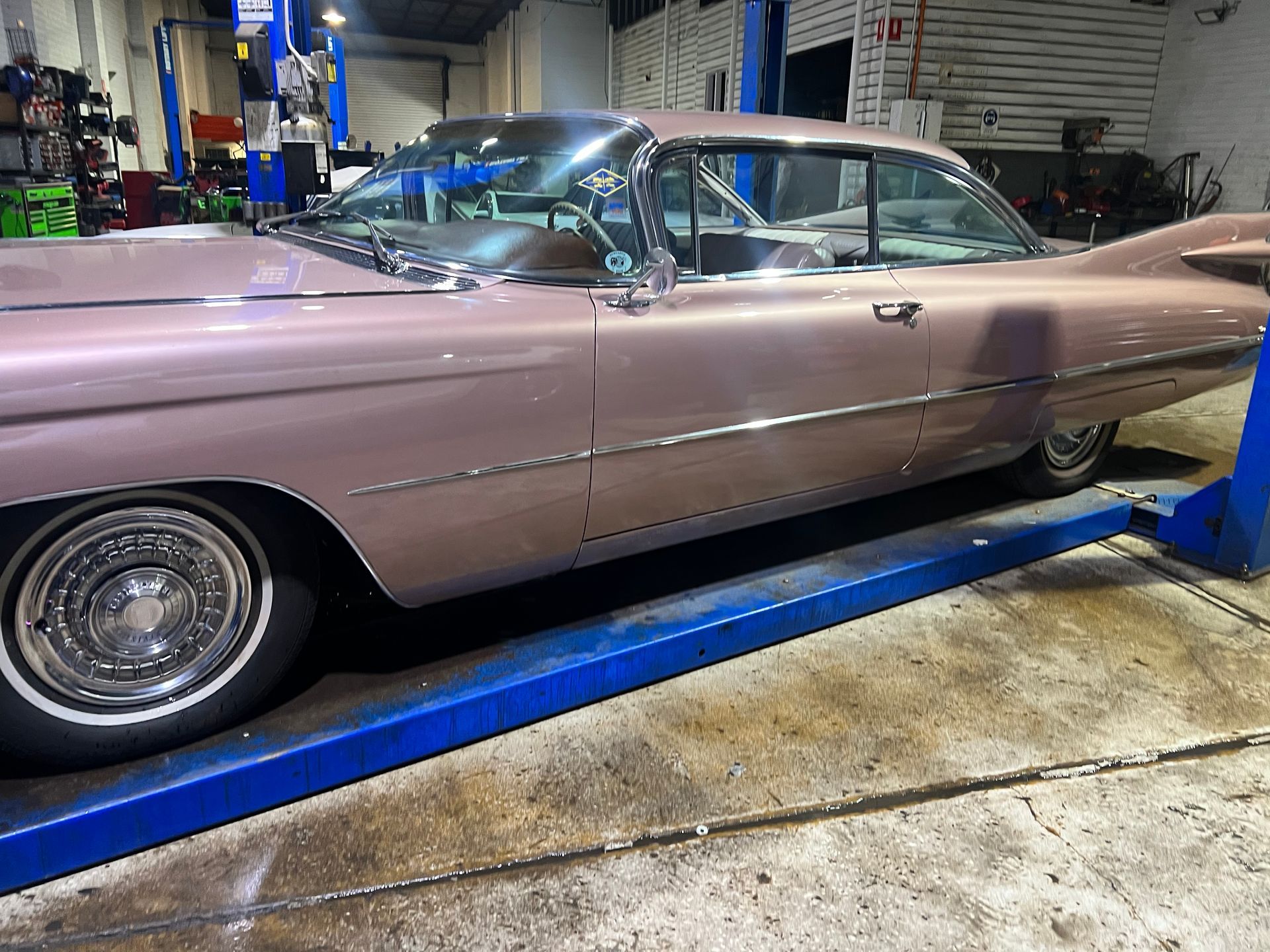 Pink Cadillac on a lift in a garage.