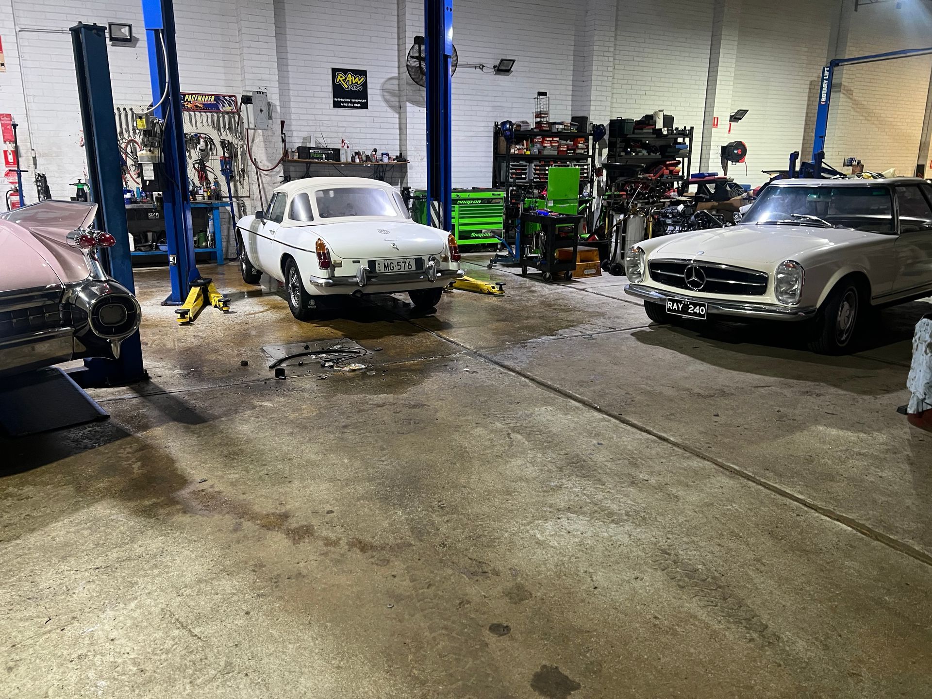 Cars inside a garage with repair equipment; a white car in the center.