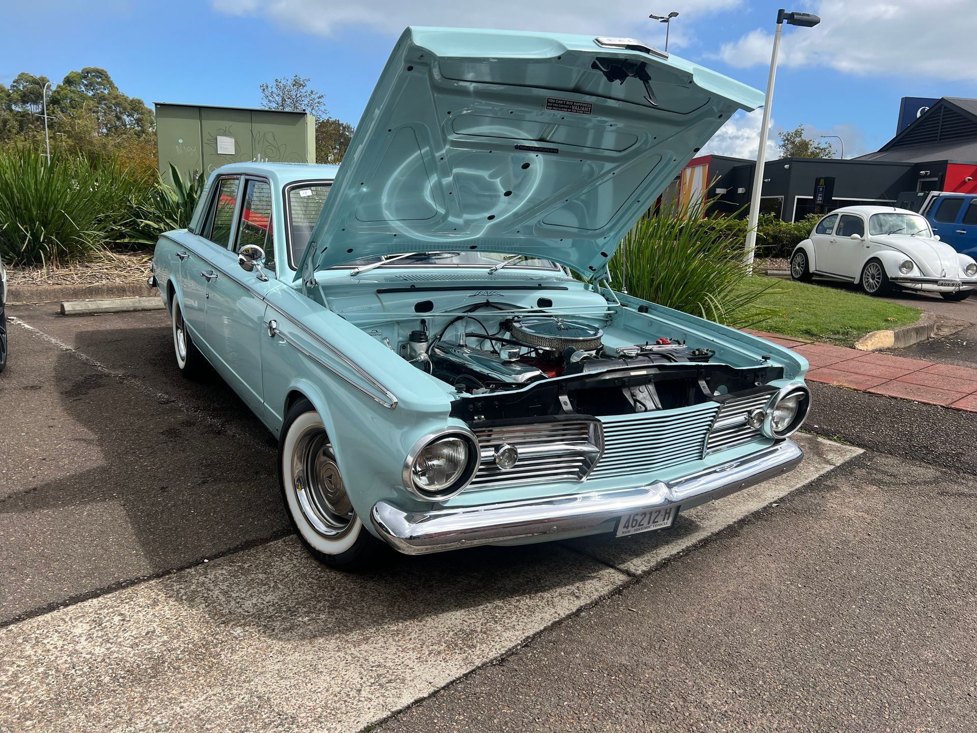 Light blue vintage car with hood up at an outdoor car show.