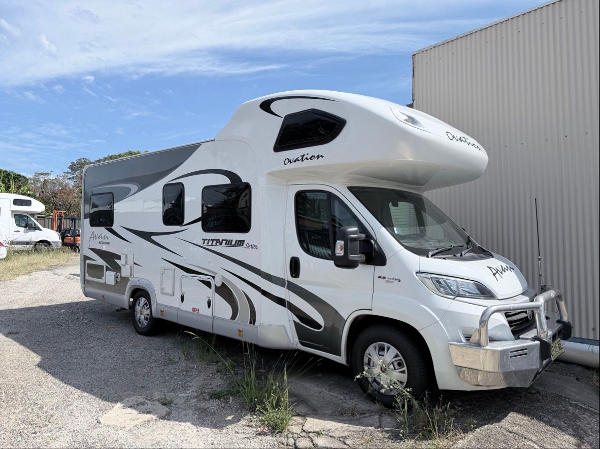 White recreational vehicle parked outside a building on a gravel lot.