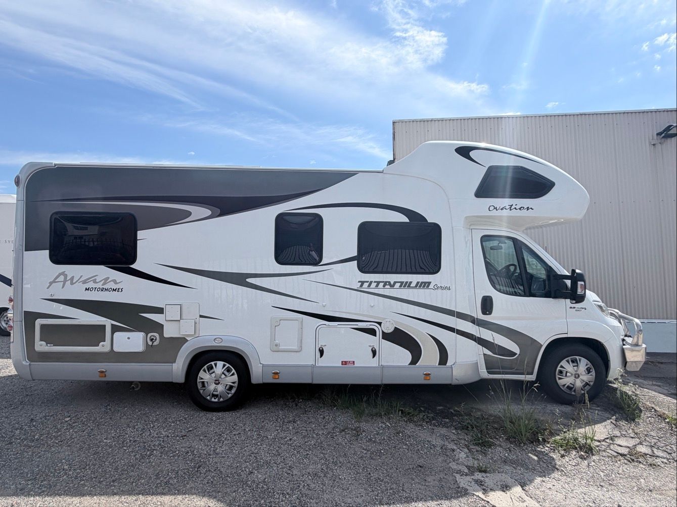 White and gray Avan motorhome parked on gravel.