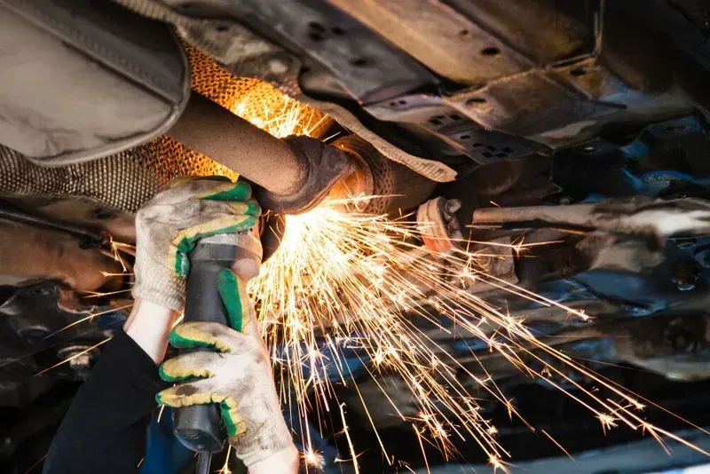 Person Using a Grinding Tool to Cut a Car Exhaust Pipe, Creating Sparks — Carline Automotive and Exhausts in Belmont, NSW
