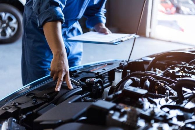 Mechanic inspecting a car engine in a garage, holding a clipboard with the hood open