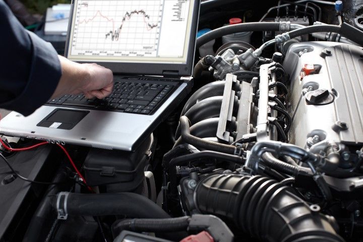 Mechanic using a laptop to diagnose a car engine in the garage