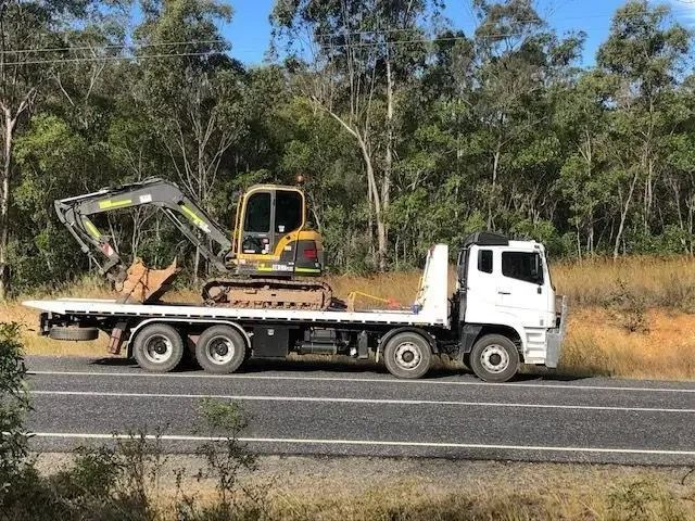 A Flatbed Truck Is Carrying An Excavator On The Back Of It — Little Mates Towing & Transport Pty Ltd In Yeppoon, QLD