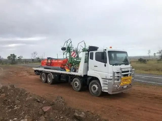 A White Tow Truck Is Driving Down A Road With A Tractor On The Back — Little Mates Towing & Transport Pty Ltd In Glenlee, QLD