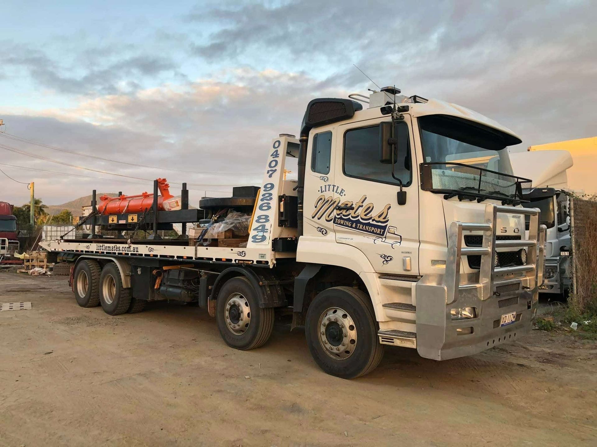 A White Truck With A Flatbed Trailer Is Parked In A Dirt Lot — Little Mates Towing & Transport Pty Ltd In Glenlee, QLD