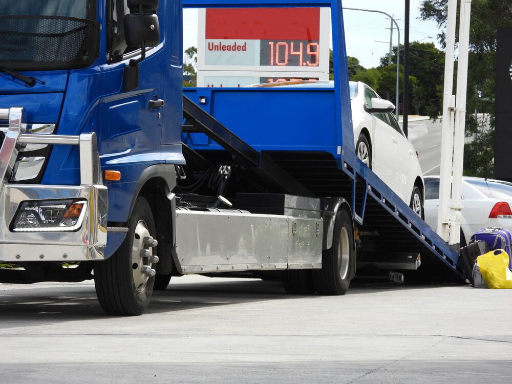 A Blue Tow Truck Is Carrying A White Car — Little Mates Towing & Transport Pty Ltd In Glenlee, QLD