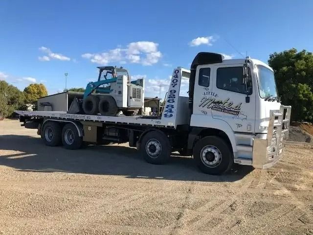 A Tow Truck Is Parked In A Gravel Lot With A Tractor On The Back — Little Mates Towing & Transport Pty Ltd In Gladstone, QLD