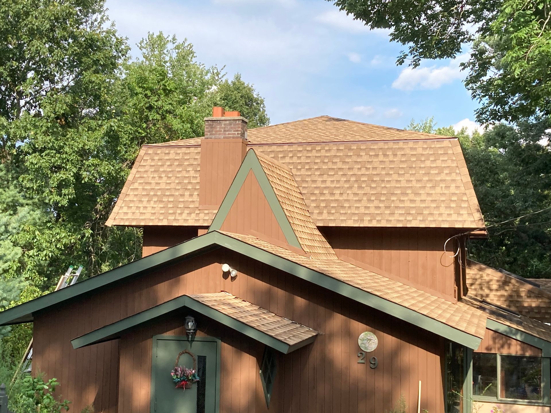 Black tiled roof on a brick house with a chimney against a blue sky.