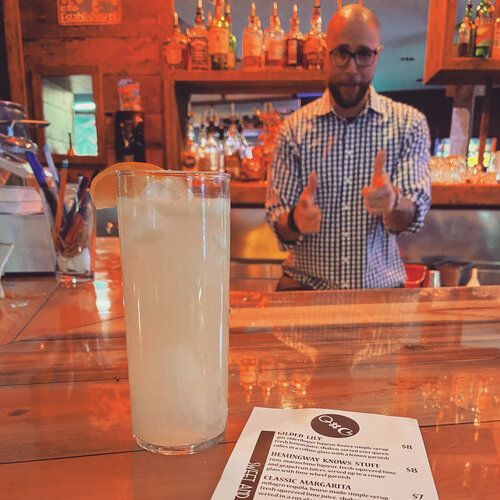 A bartender giving a thumbs up next to a tall glass of liquid