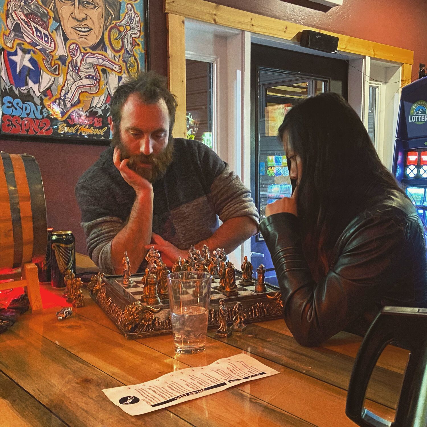 A man and a woman are playing chess at a bar