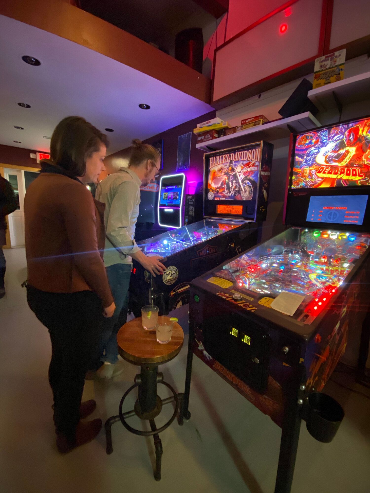 A group of people are playing pinball machines in a room.
