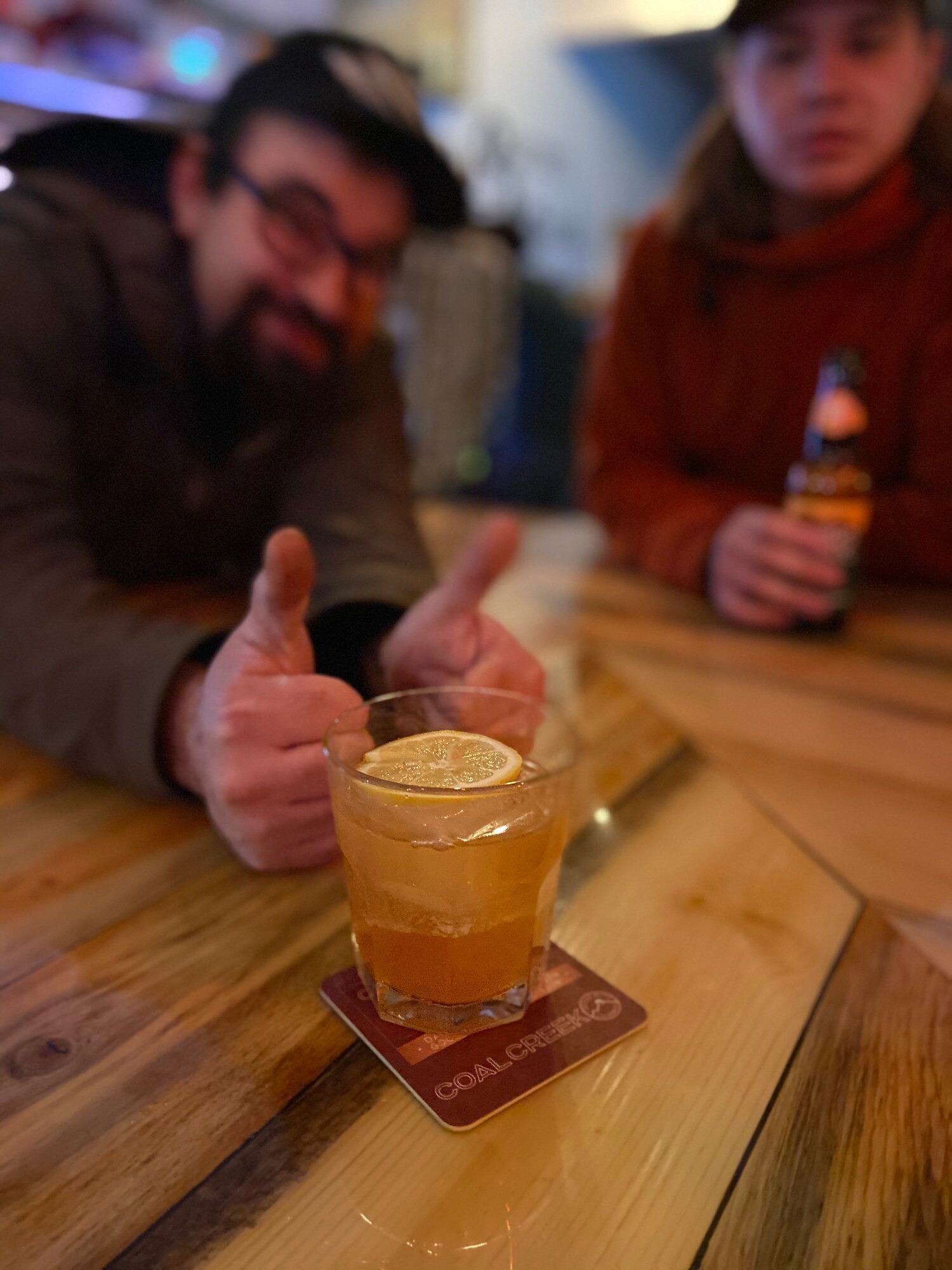 A man is giving a thumbs up next to a drink on a coaster.