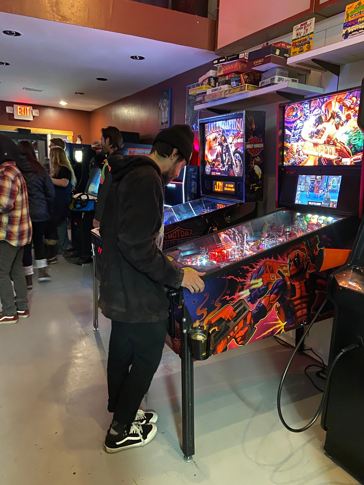 A man is playing a pinball machine in an arcade.