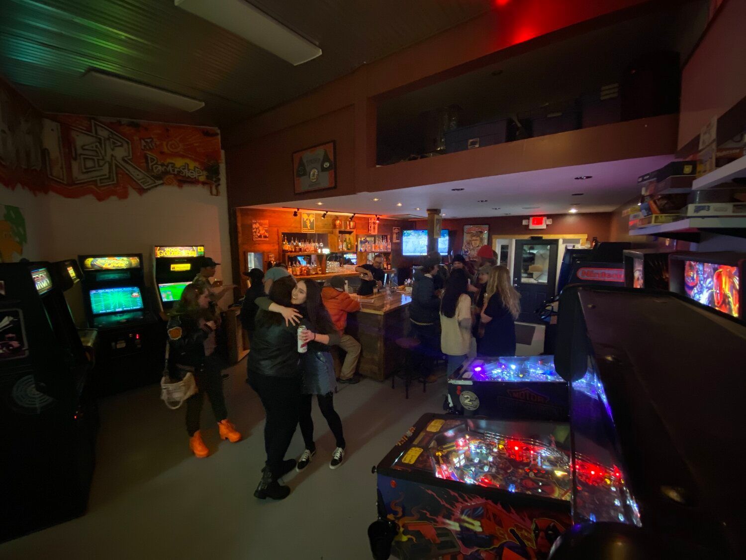 A group of people are standing in a room filled with arcade games.