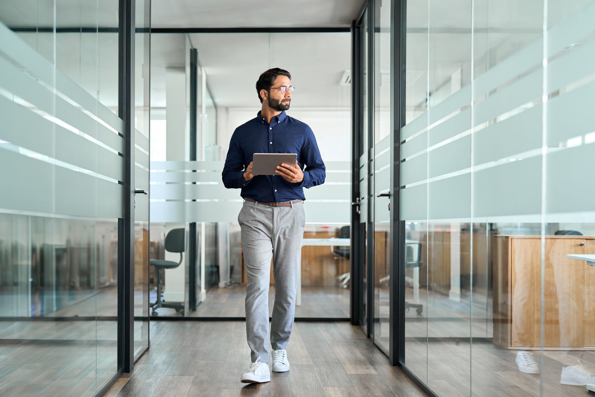 Man holding a tablet in a glass-walled office hallway
