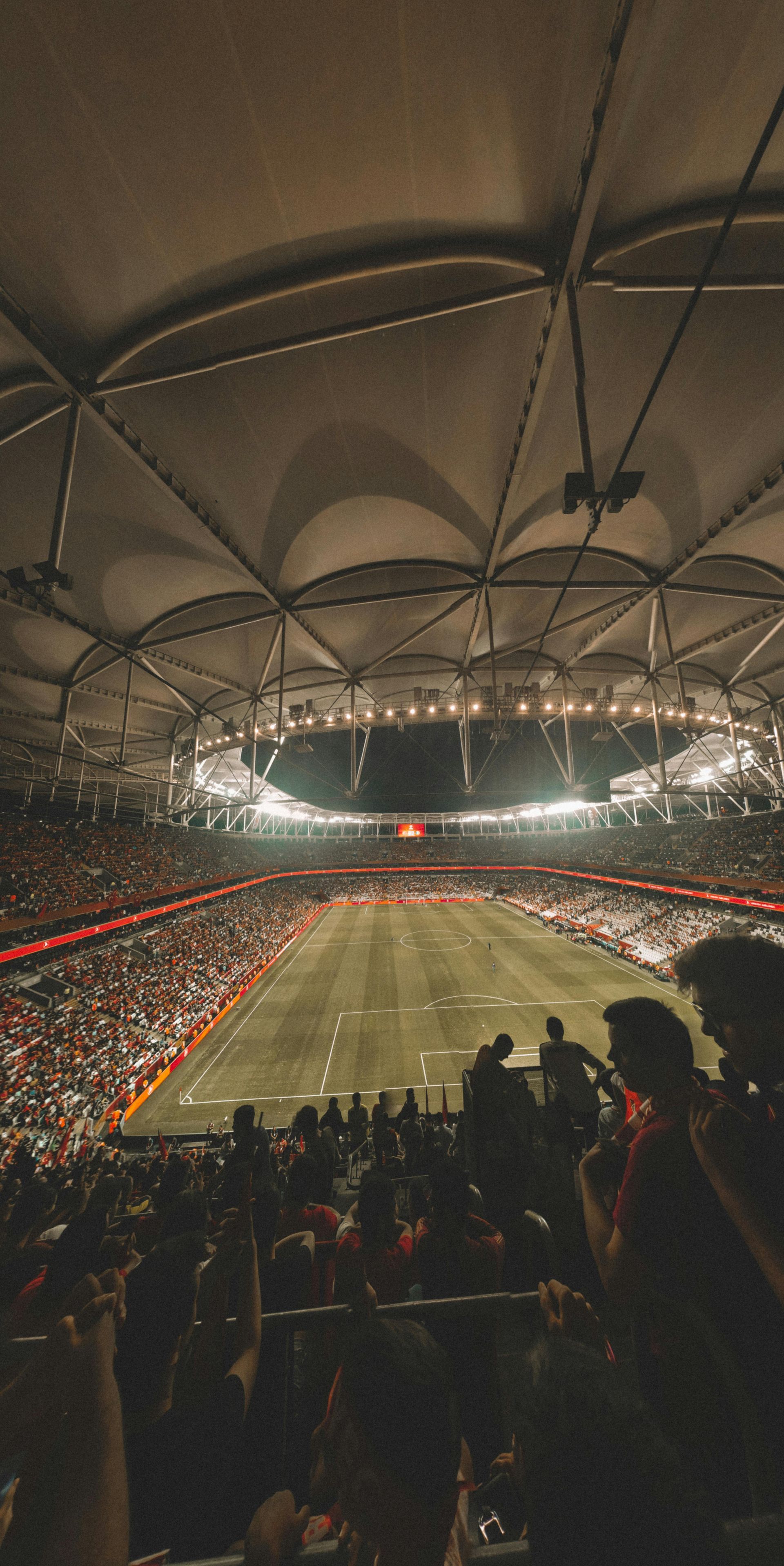 Packed soccer stadium under a glowing domed roof at night, viewed from the stands.