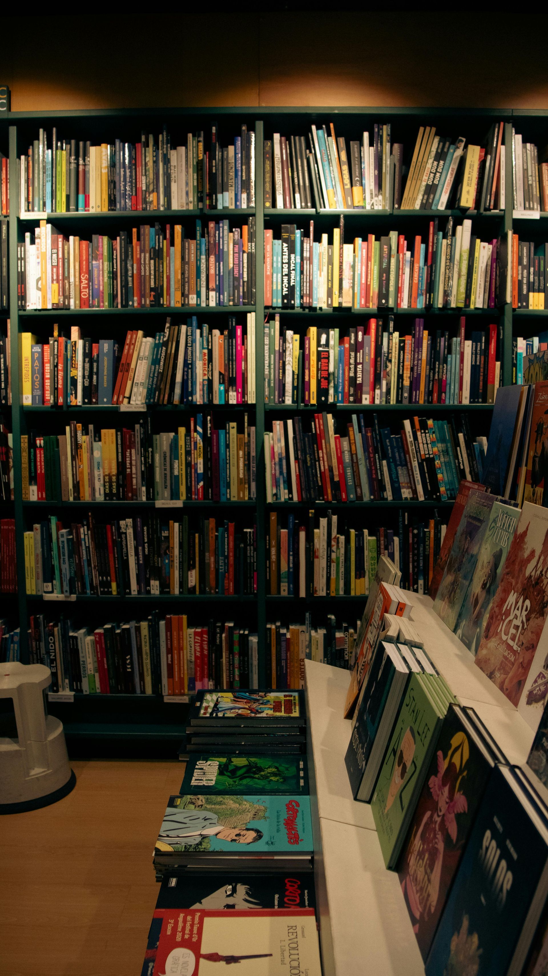 Bookstore aisle with tall shelves of colorful books and a display rack in the foreground.