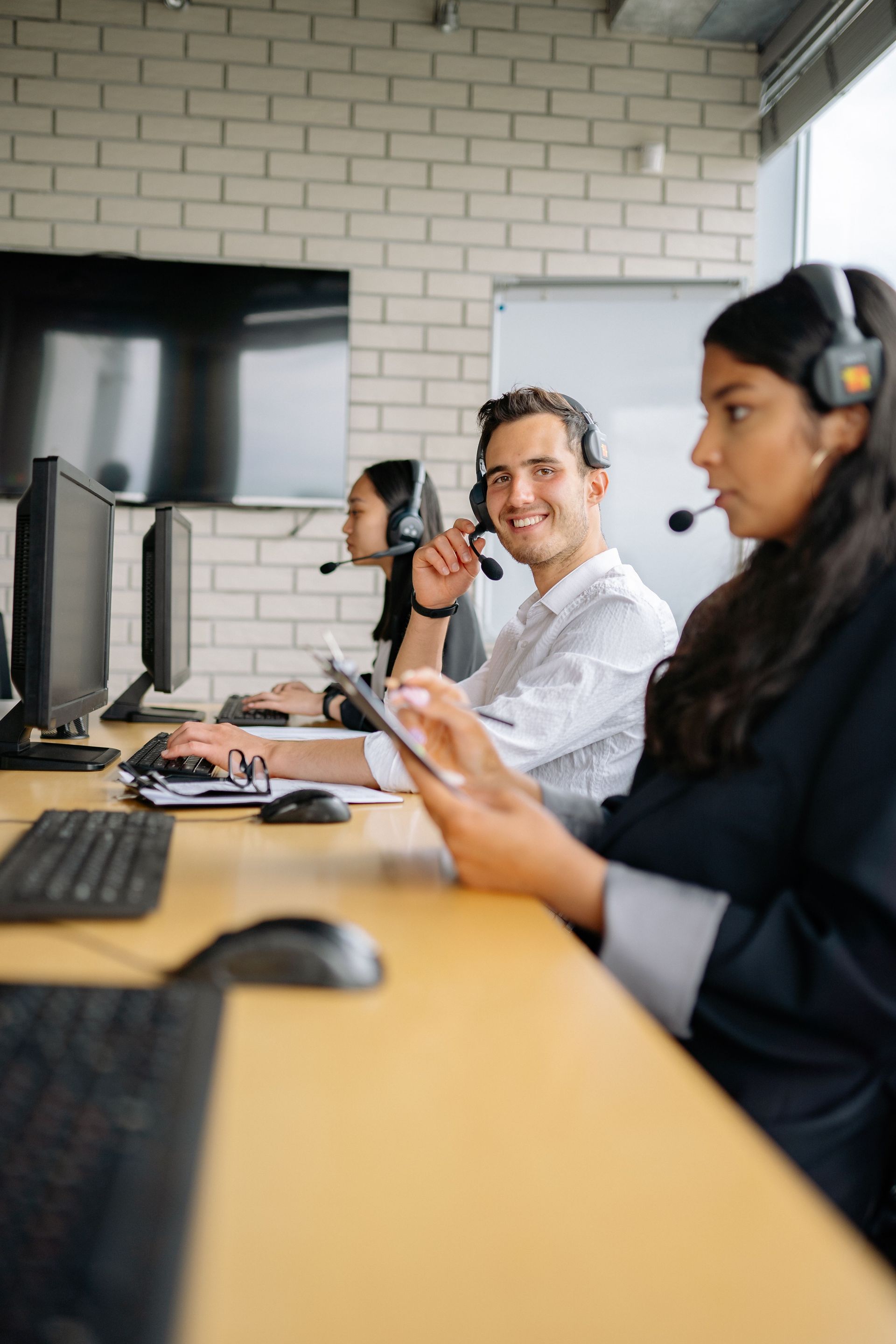 Colleagues wearing headsets in a modern office, one giving a thumbs-up at a desk with computer monitors.