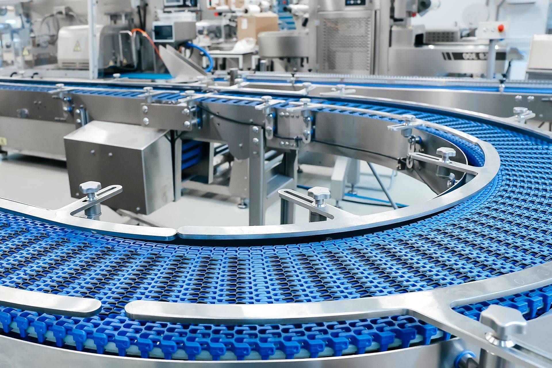 A blue plastic modular conveyor belt curves through a stainless steel industrial production line.